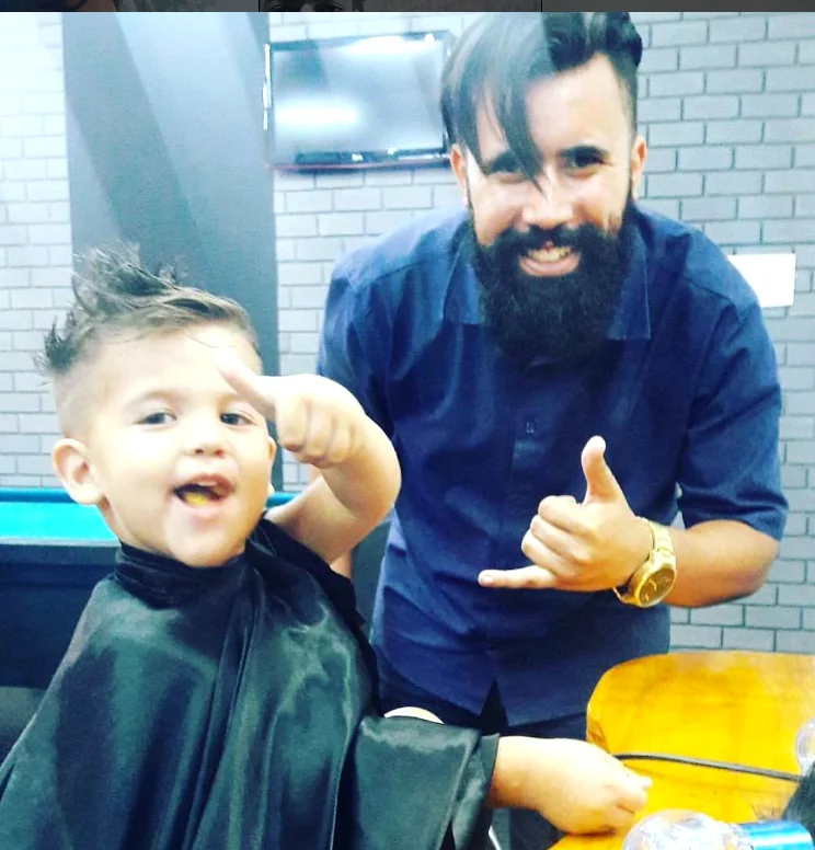 Thomas Gabriel sorrindo ao lado de uma criança atendida na barbearia